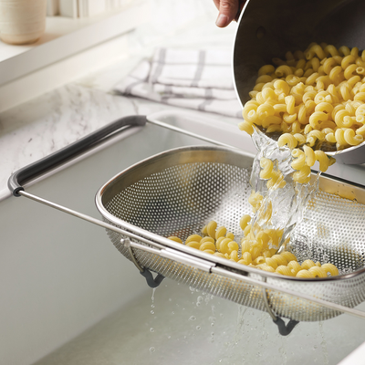 A person drains pasta through a colander in a kitchen sink.