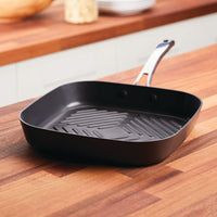 The 11-Inch Cook + Create Hard Anodized Nonstick Deep Grill Pan sits elegantly on the wooden kitchen countertop, showcasing its hard anodized aluminum construction.