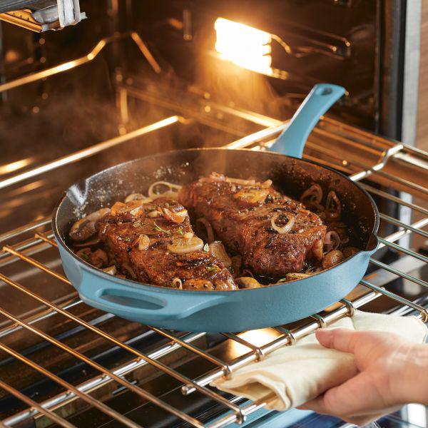 Steaks sizzling in a 12-Inch NITRO Cast Iron Skillet inside an oven.