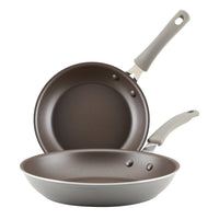 The two frying pans from the 2-Piece Cook + Create Nonstick Frying Pan Set, crafted in gray aluminum with handles and gleaming nonstick surfaces, are neatly stacked one above the other.