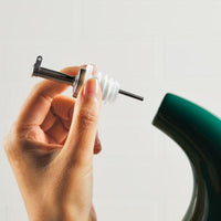 A hand delicately holds a precision pouring stopper near a green 24-Ounce EVOO Bottle, perfectly suited for extra virgin olive oil or wine.