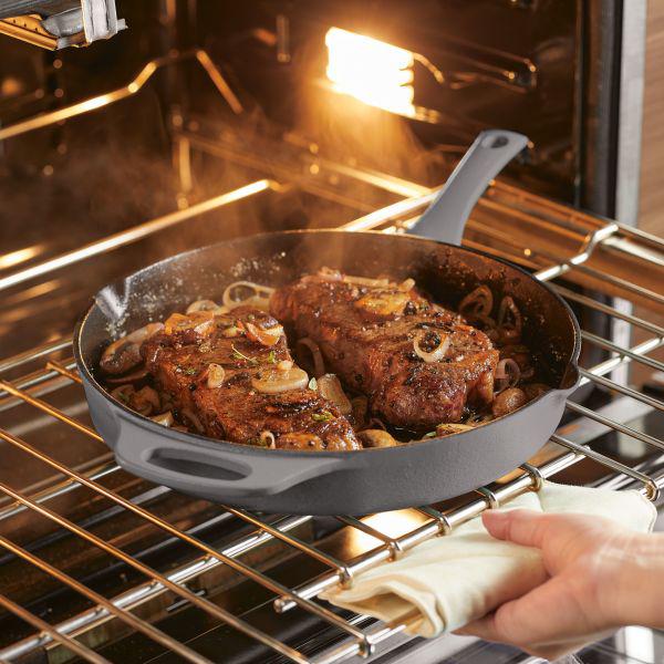 The 12-Inch NITRO Cast Iron Skillet cooks steak and onions to perfection, evenly distributing heat in the oven's cozy embrace.