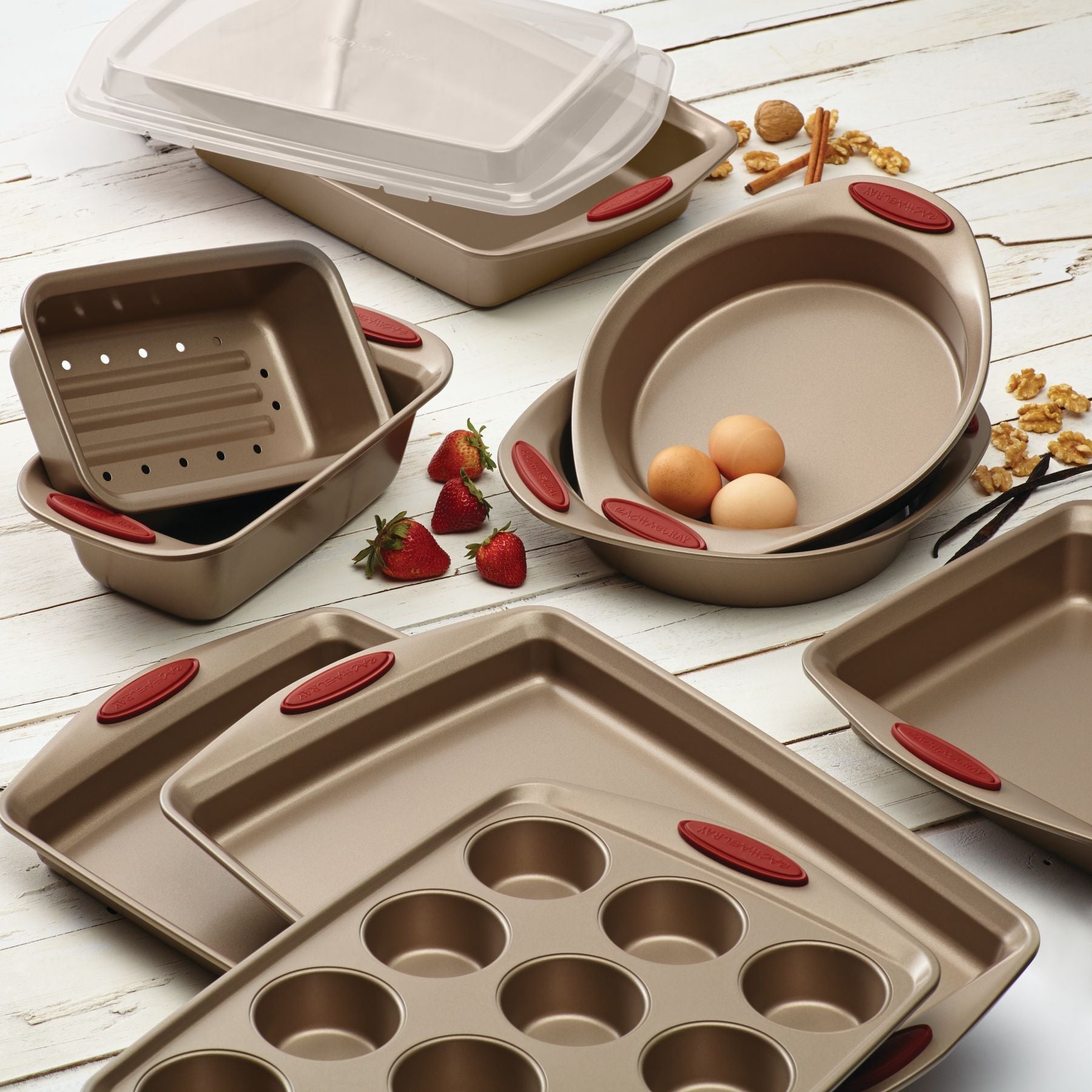 A 10-Piece Nonstick Bakeware Set featuring red handles and surrounded by ingredients on a white table.
