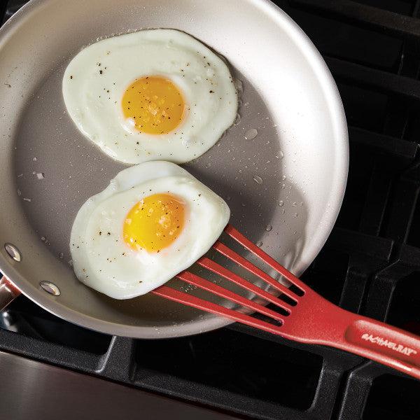 Two fried eggs sizzle in the pan, while a trusty kitchen tool—a red spatula from the 10-Inch & 12-Inch Nylon Spatula Set—rests on the stove.