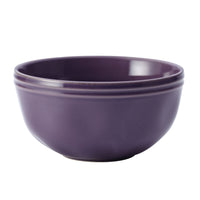 The 16-Piece Dinnerware Set includes a purple ceramic bowl with smooth edges and a glossy finish, boasting a handcrafted texture that adds uniqueness to your collection.